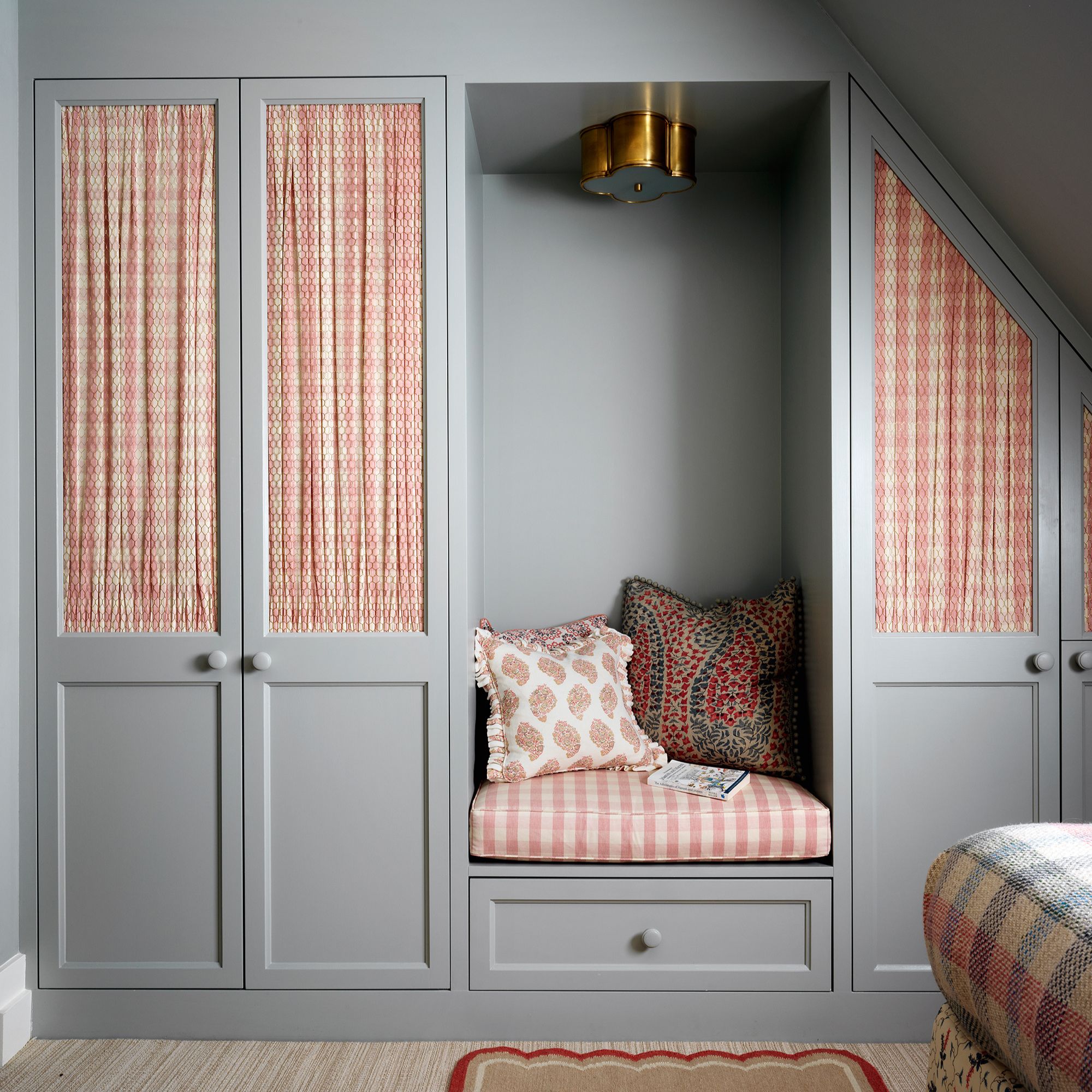grey built-in wardrobe and seating area with pink and white gingham fabric panels in loft conversion