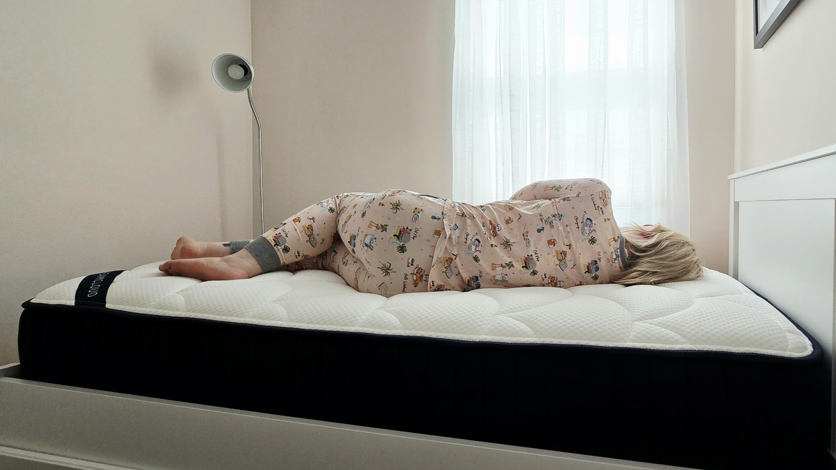 Mattress tester in cat pajamas rests on her side for the DreamCloud Classic Memory Foam Mattress review