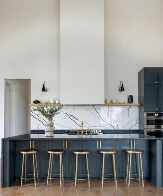 Kitchen with blue cabinets, island with stools, stone backsplash, shelf above and cathedral ceiling