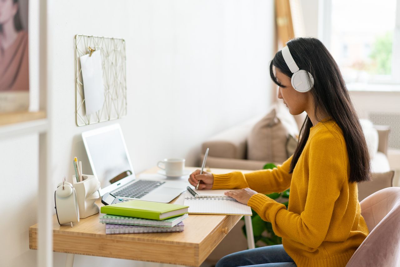 Adult learning online at home. Handwriting in notebook while listening to lecture in headphones