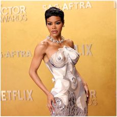 a black woman with short hair poses in a strapless gown in front of a yellow background
