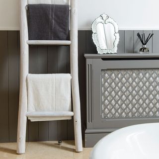 Grey radiator cover in bathroom next to whitewashed wooden towel rail