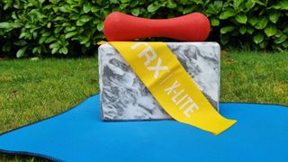 Image shows a yellow TRX Strength Band on a blue yoga mat resting on a yoga block and a red weight.