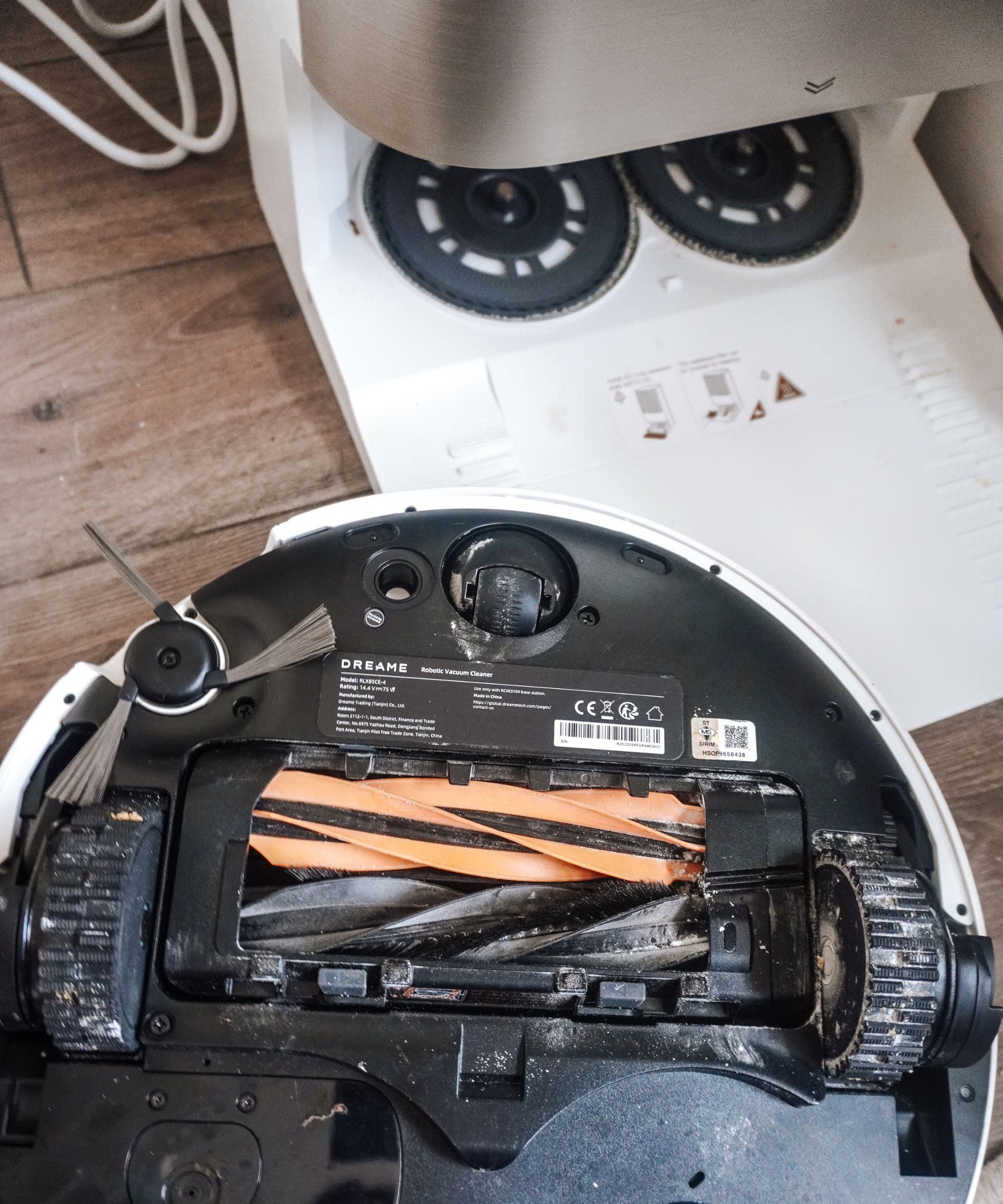 An upside down Dreame X50 Ultra robot vacuum cleaner next to a white and silver base station