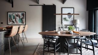 interior of open plan kitchen diner with black vaulted ceiling, kitchen island with breakfast bar, round dining table and black chairs, black sliding barn door