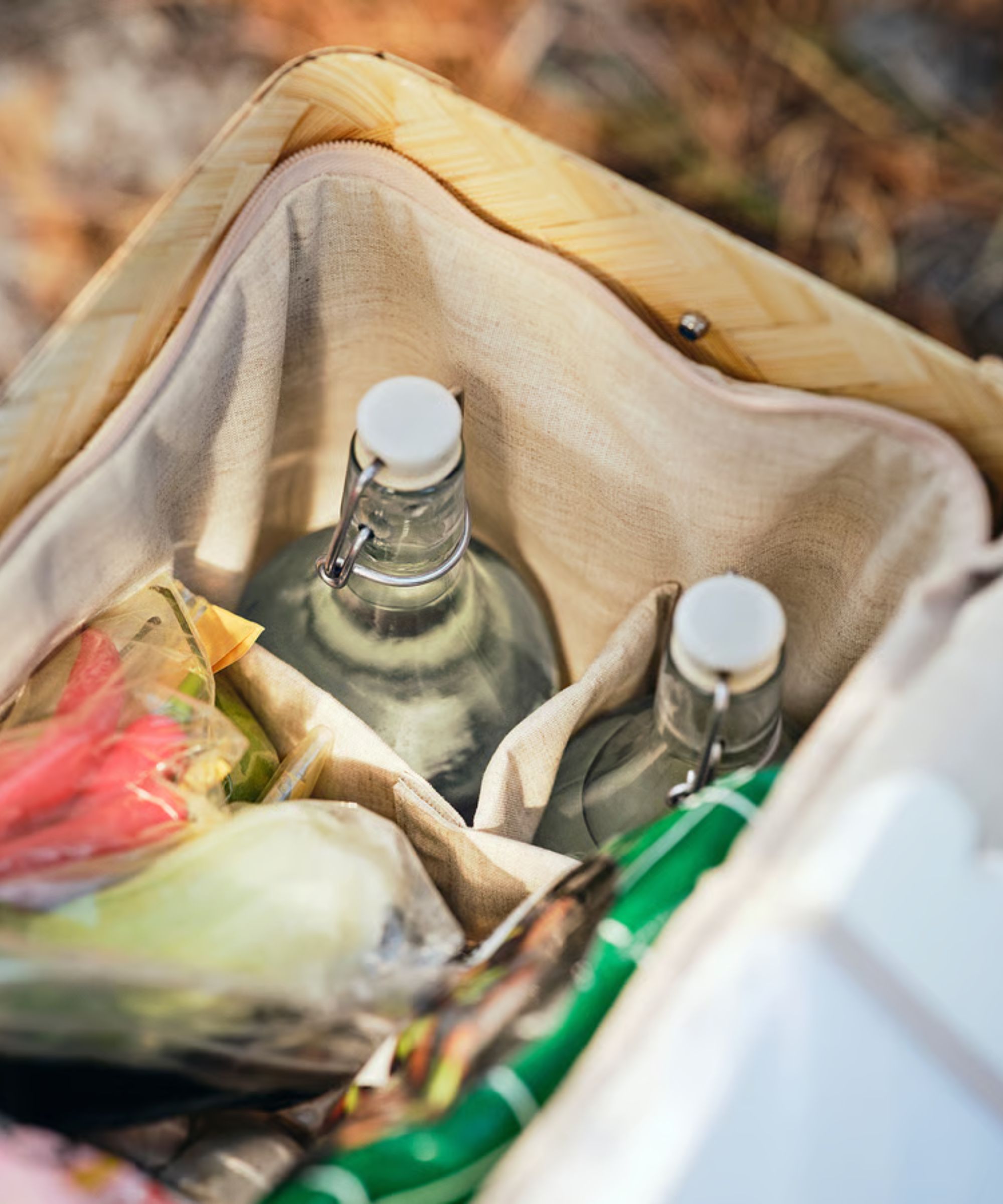 The inside of a bamboo cooler basket, with a fabric cool bag, two glass bottles of water, and some bagged snacks