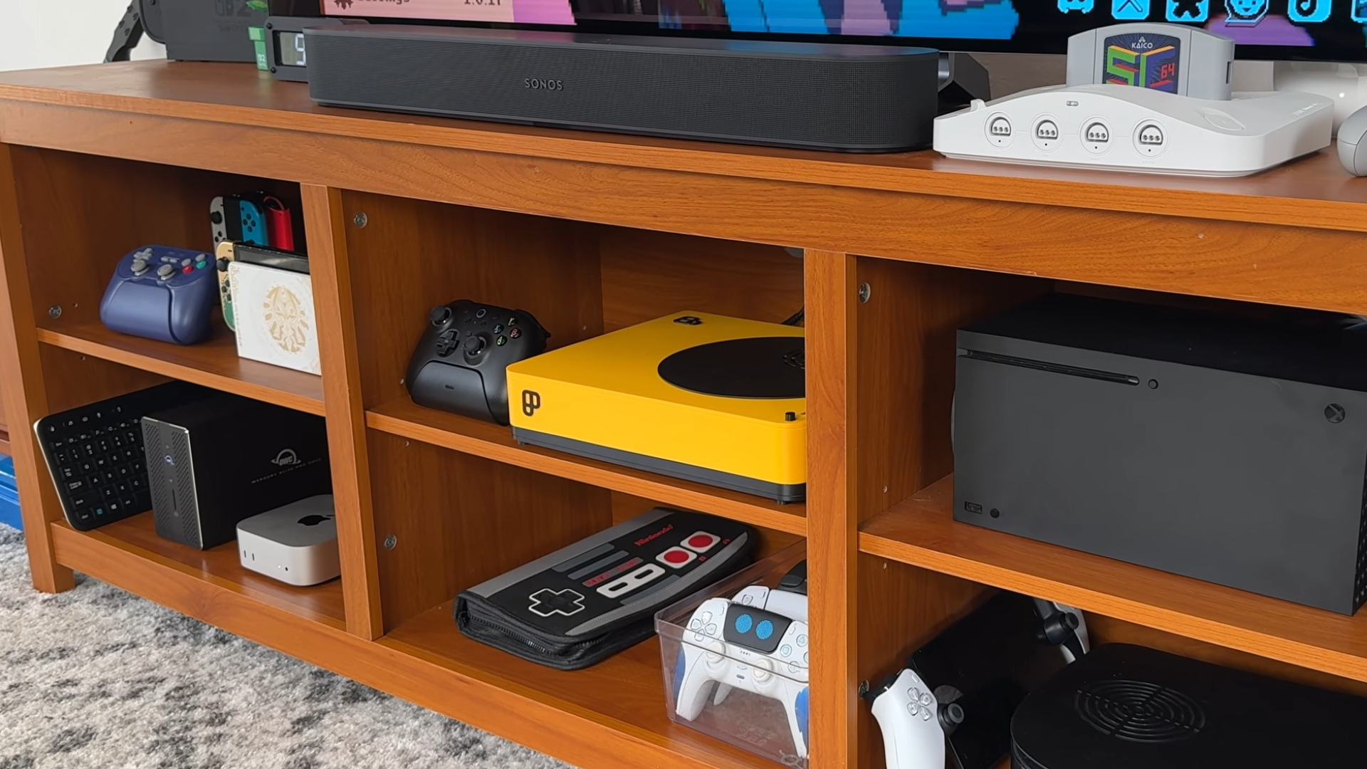 A Playnix Console underneath a TV surrounded by traditional consoles and controllers