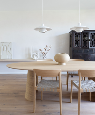 Oval wooden dining table in modern room with white decor and black cabinet in the background