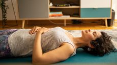 Woman lies on an exercise mat with her hands over her diaphragm and eyes closed