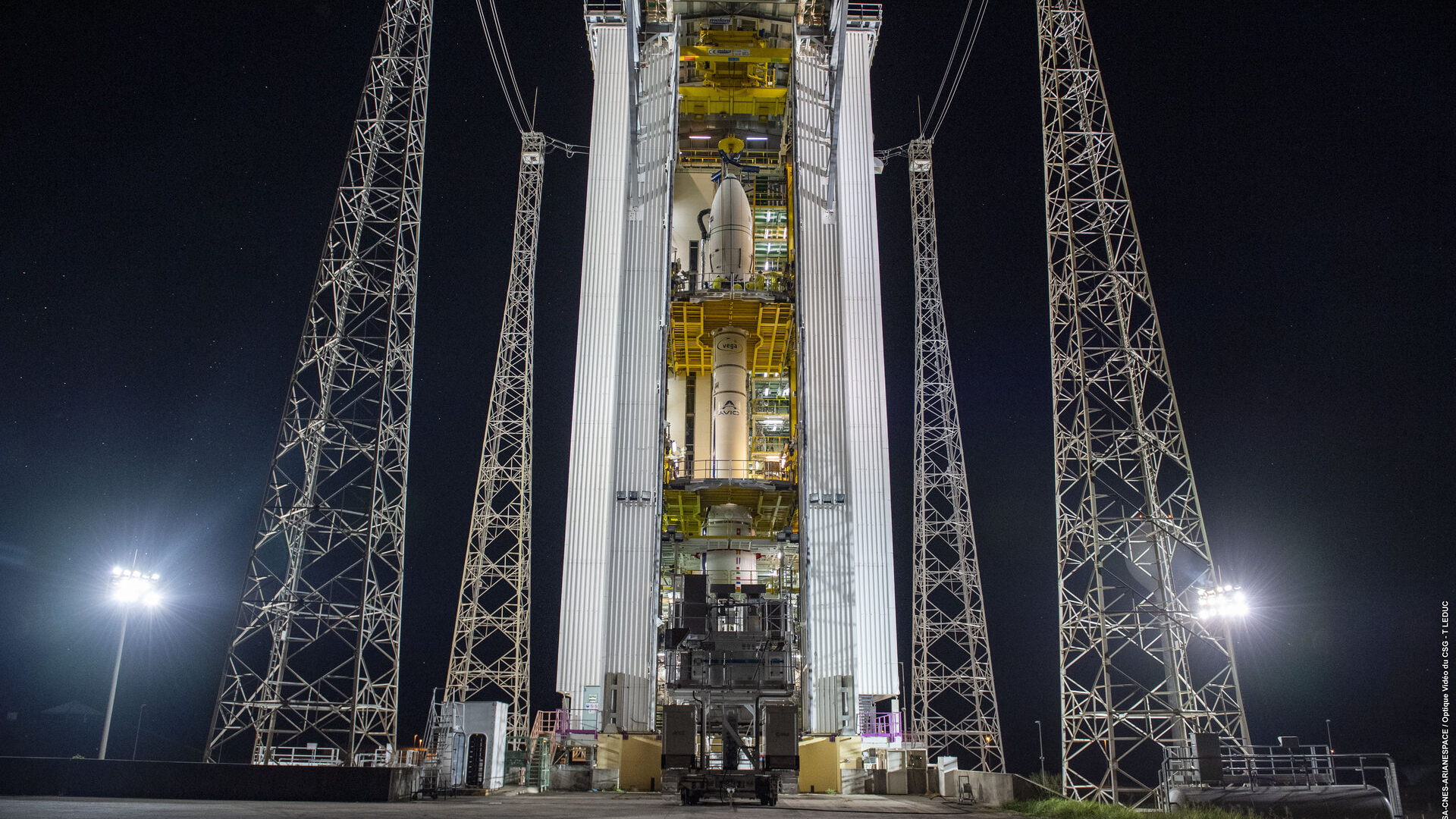 A white rocket surrounded by its hangar and scaffolding before launch.