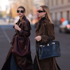 Two women crossing the street wearing brown trench coats with a clean-girl aesthetic, fitting for a powdery perfume look