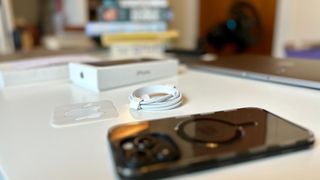 an iphone 15 pro, usb-c cable, apple sticker, and an iPhone boxed arranged on a desk