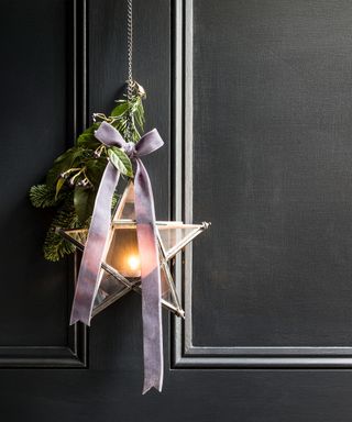 Black door decorated with star lantern decoration, foliage and ribbon