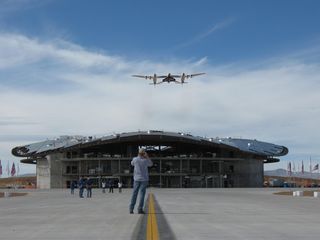The Virgin Galactic suborbital vehicle SpaceShipTwo, called Enterprise, soars over New Mexico's Spaceport America terminal – still under construction – under the belly of its huge mothership WhiteKnightTwo during the spaceport’s runway dedication ceremony