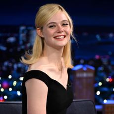 Elle Fanning smiles at the camera wearing a black dress