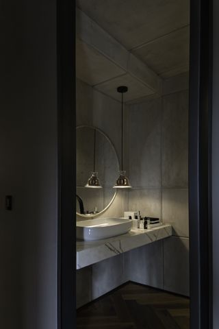 powder room with parquet wood floor, marble countertop, white basin, round mirror, pendant light