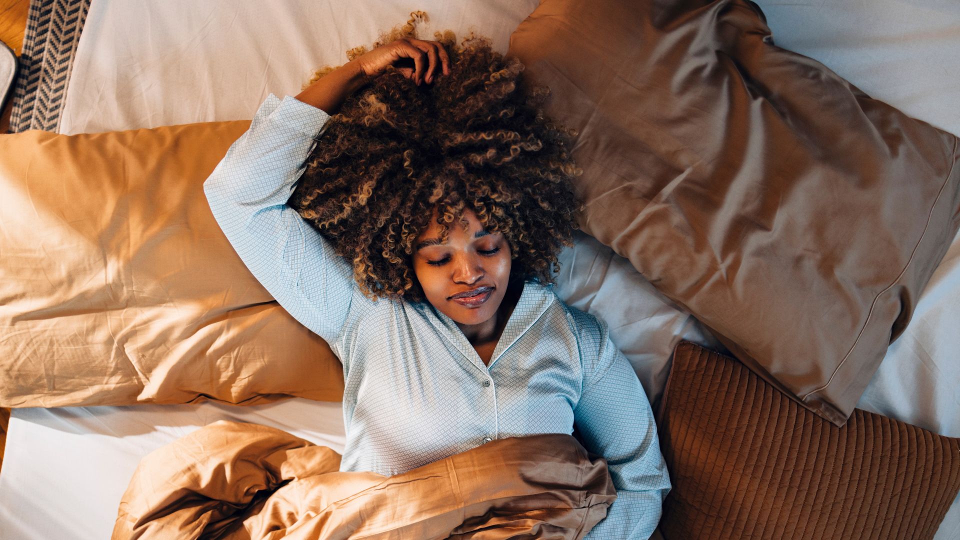 Woman lying on back in bed around pillows with light on, learning how to fall asleep in 3 minutes