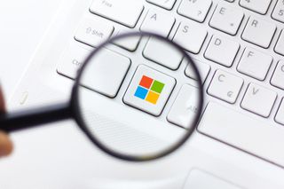 Microsoft logo under magnifying glass, which appears in color in place of the Windows key on a standard white Microsoft keyboard