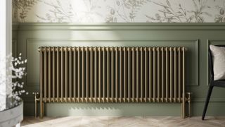 Gold radiator on a wall with half green paneling and half floral wallpaper