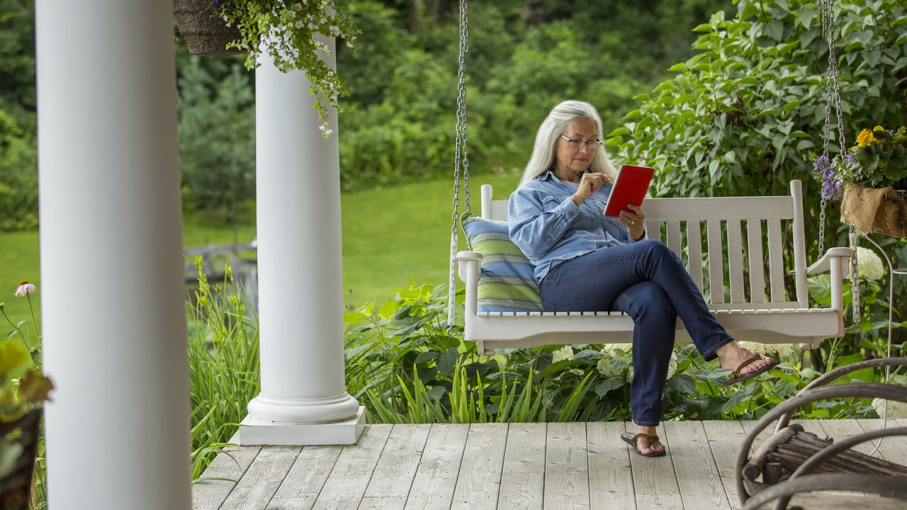 An older woman sits on a porch swing and reads.