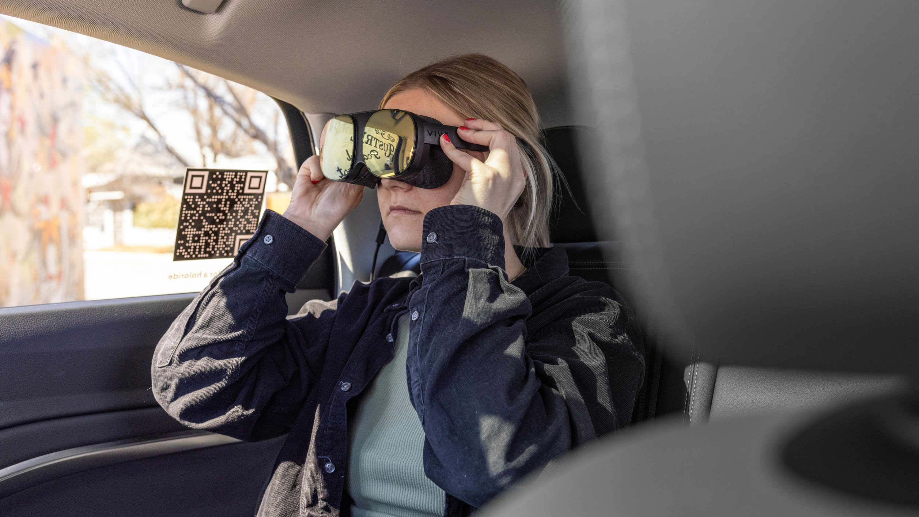 Young woman sitting in rear seat of car, while wearing a VR headset