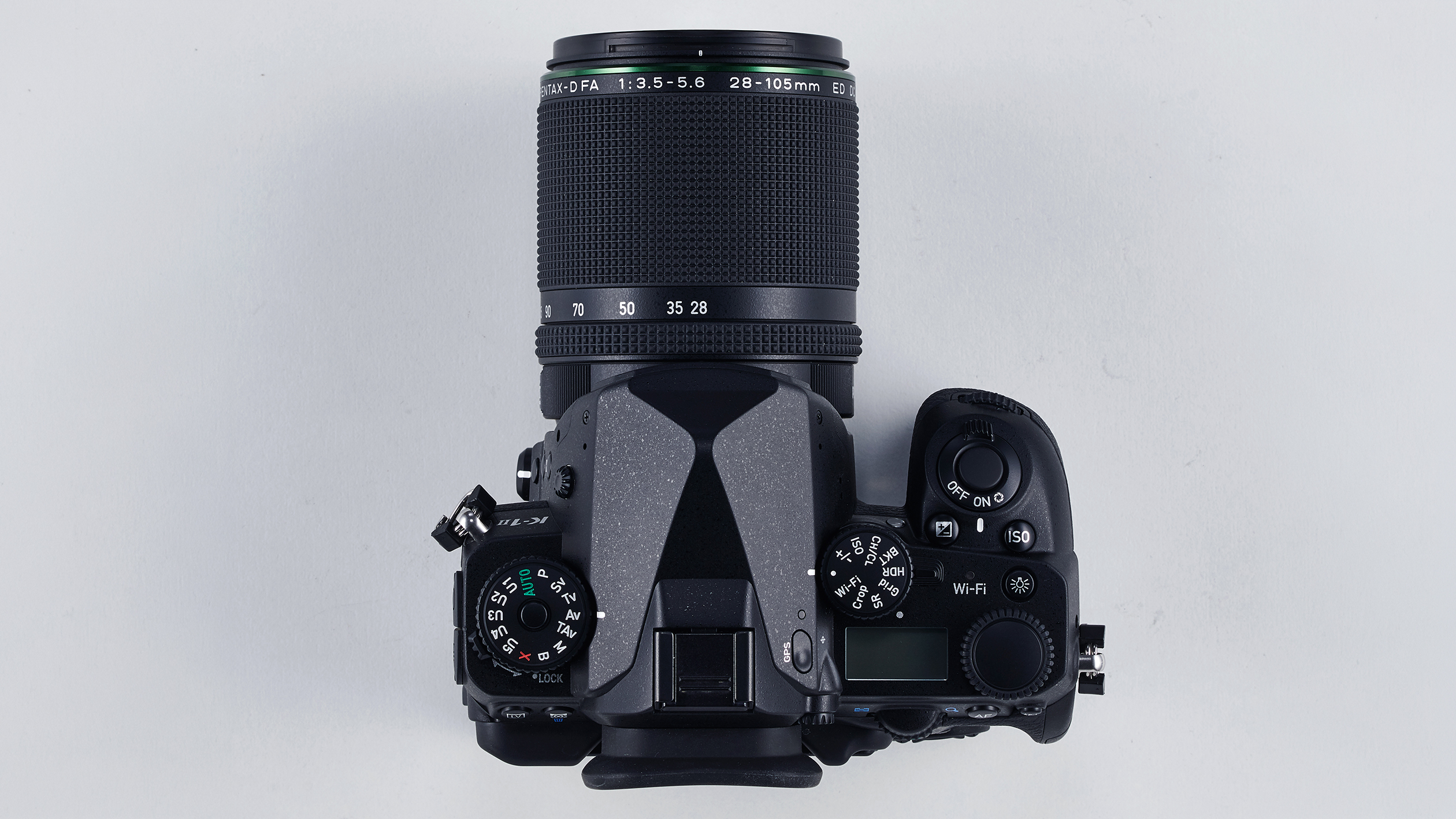 Top view of a black DSLR camera with a Pentax 28-105mm zoom lens attached on a light gray background