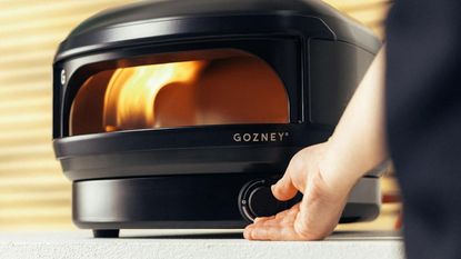 The black Gozney Arc Lite gas powered pizza oven being turned up by a mans hand.