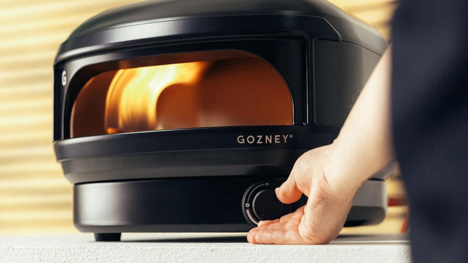 The black Gozney Arc Lite gas powered pizza oven being turned up by a mans hand. 