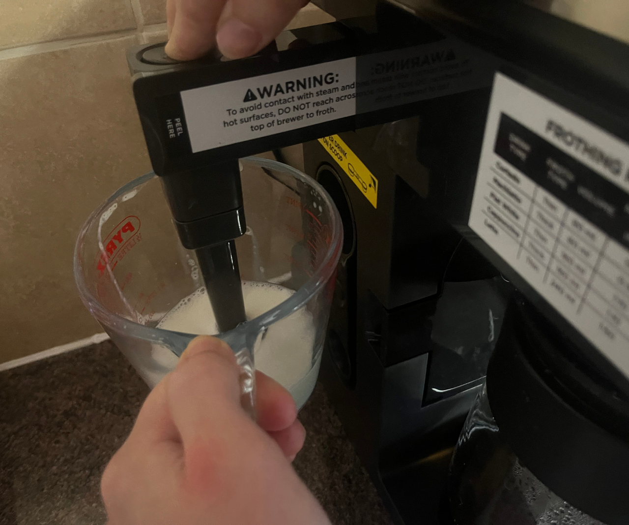 Someone frothing milk in a glass job using the side frother attachment of a drip coffee maker.