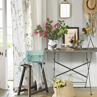 room with white wall flower vase on table wooden table with door with curtain and flowers in bag
