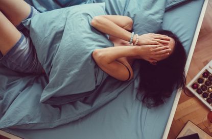 Woman lying in bed with her hands covering her face