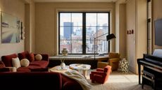 A small living room apartment with a red L-shaped sofa, a piano, and off-white walls