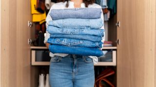 Woman carrying several pairs of folded jeans