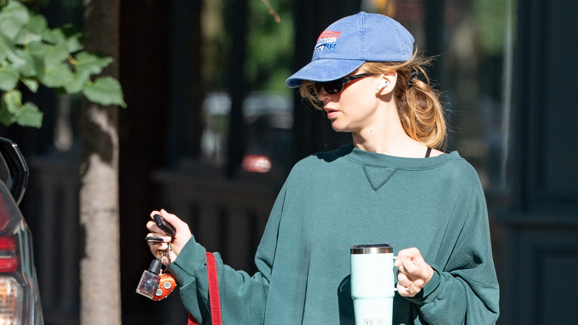 Jennifer Lawrence wearing a green sweatshirt, capri leggings, Adidas slides and a blue baseball cap in NYC.