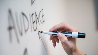 A hand writing the word Audience on a whiteboard