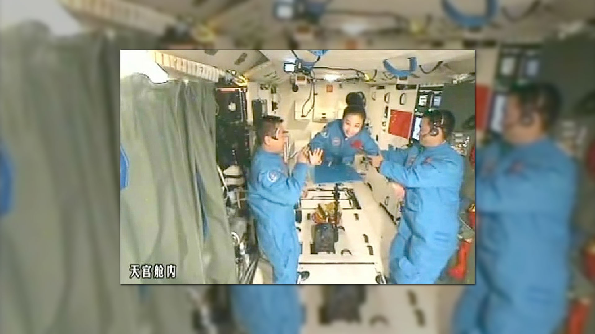 two men and a woman in matching blue coveralls float inside a space lab