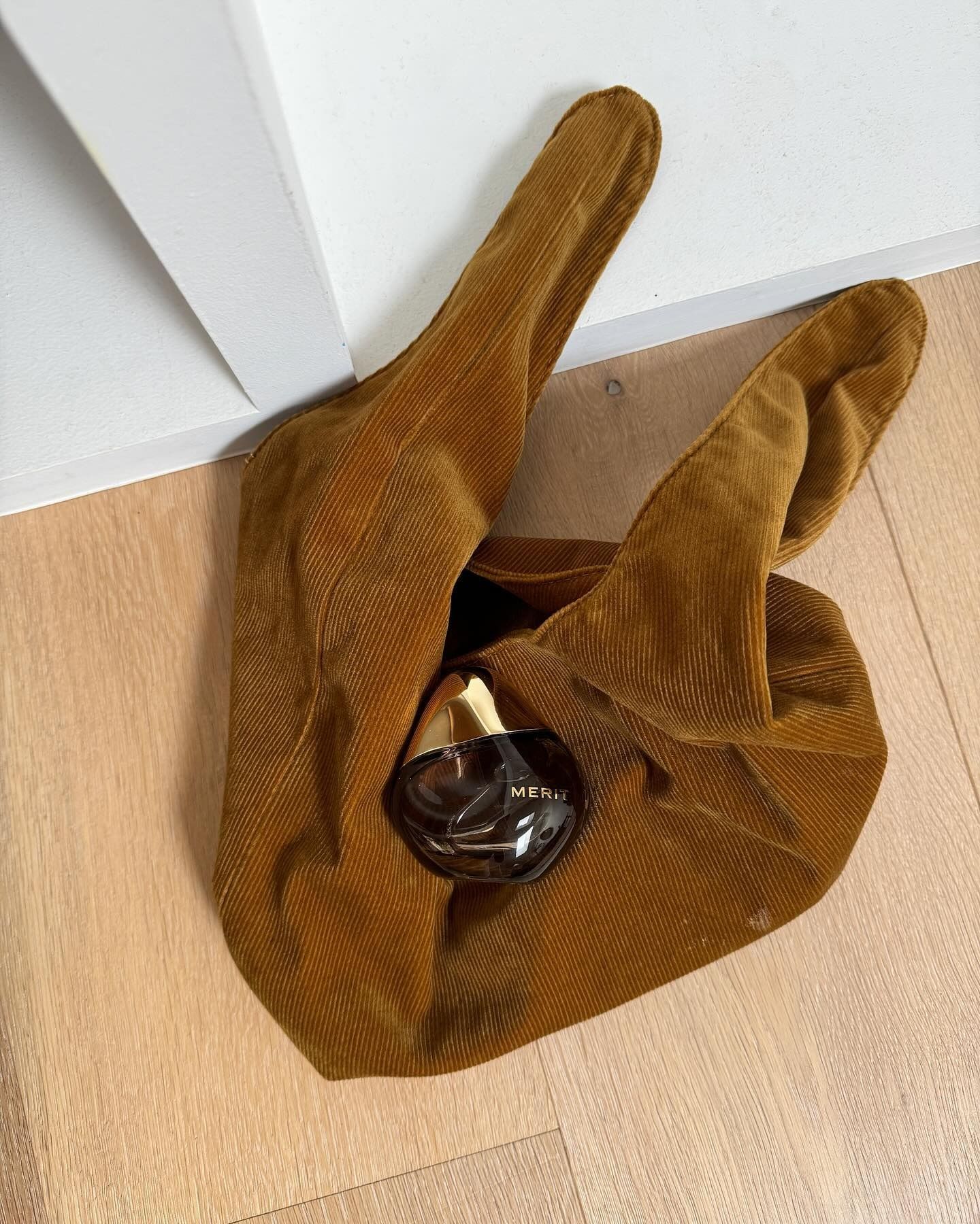 The Merit Retrospect perfume perched on top of a stylish brown bag