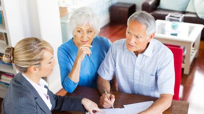 An older couple sign papers with their financial adviser.