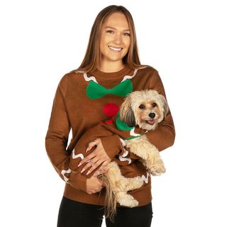 A person wearing a brown gingerbread Christmas sweater while they're holding their dog wearing the same gingerbread Christmas sweater, for Christmas sweaters for dogs.
