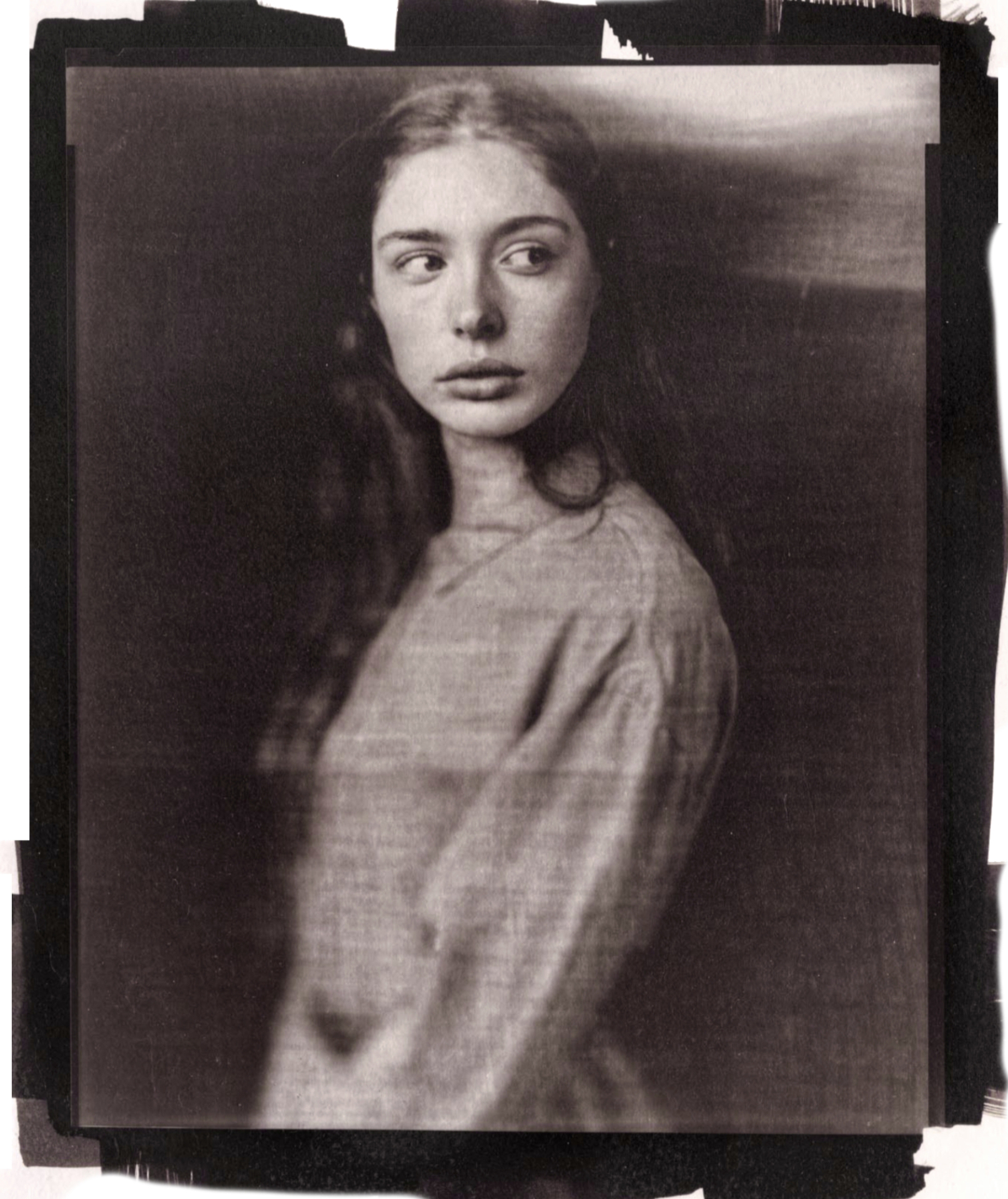 A vintage, faded photo of a person wearing a simple, loose-fitting garment, captured in soft focus with a moody atmosphere