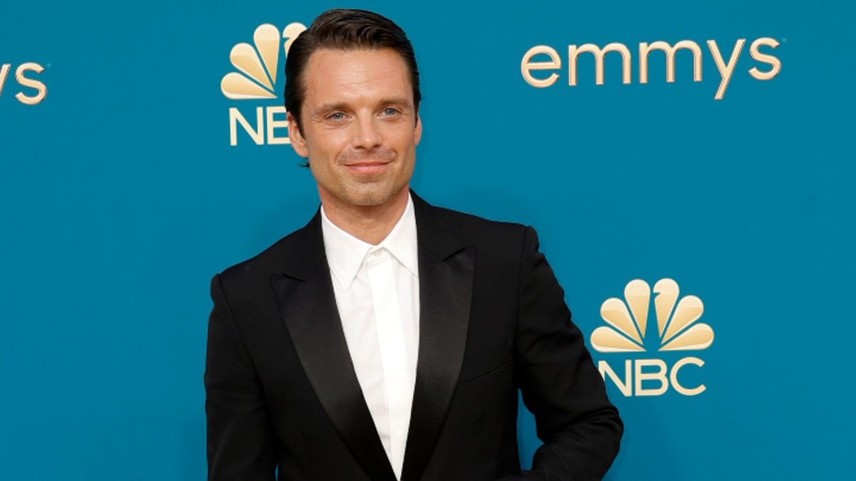 Sebastian Stan walks the carpet at the emmys in a black suit and white button down with no tie.