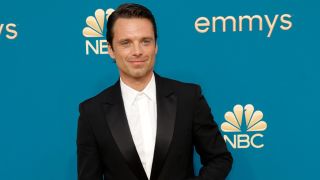 Sebastian Stan walks the carpet at the emmys in a black suit and white button down with no tie.
