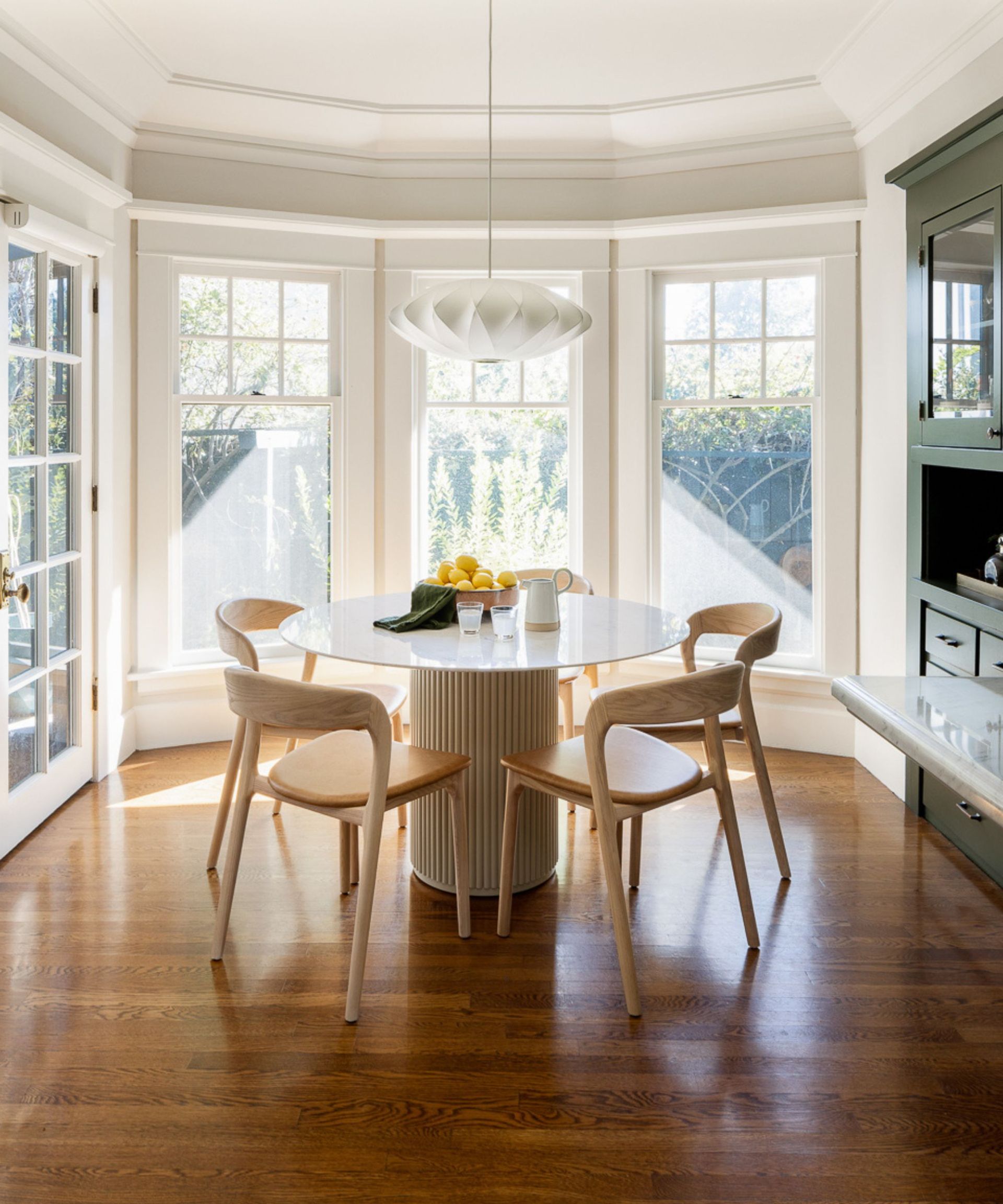 Dining room with large windows, crown moulding and round marble coffee table with wood chairs