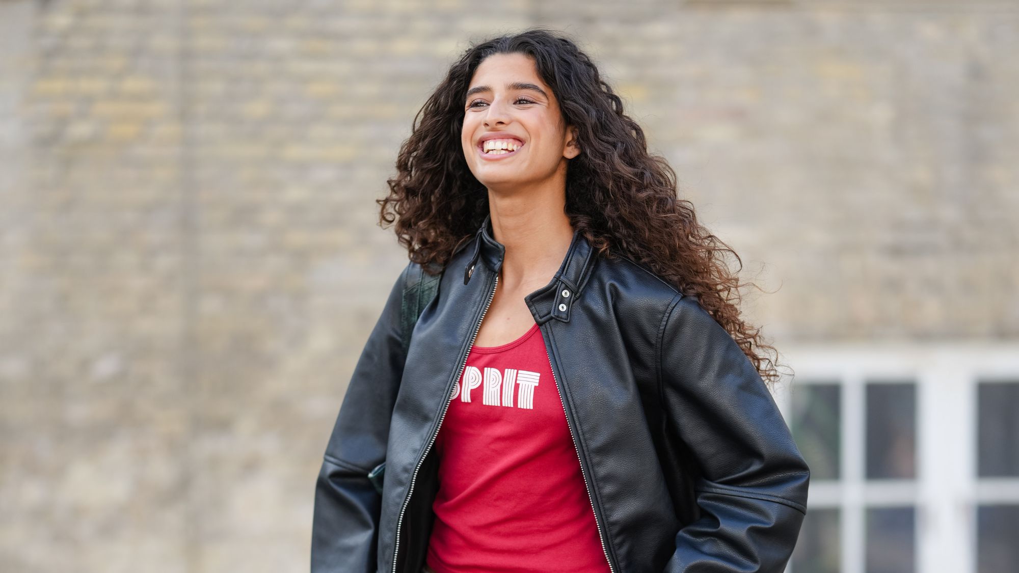 woman with long curly brown hair wearing black leather jacket and red tank top
