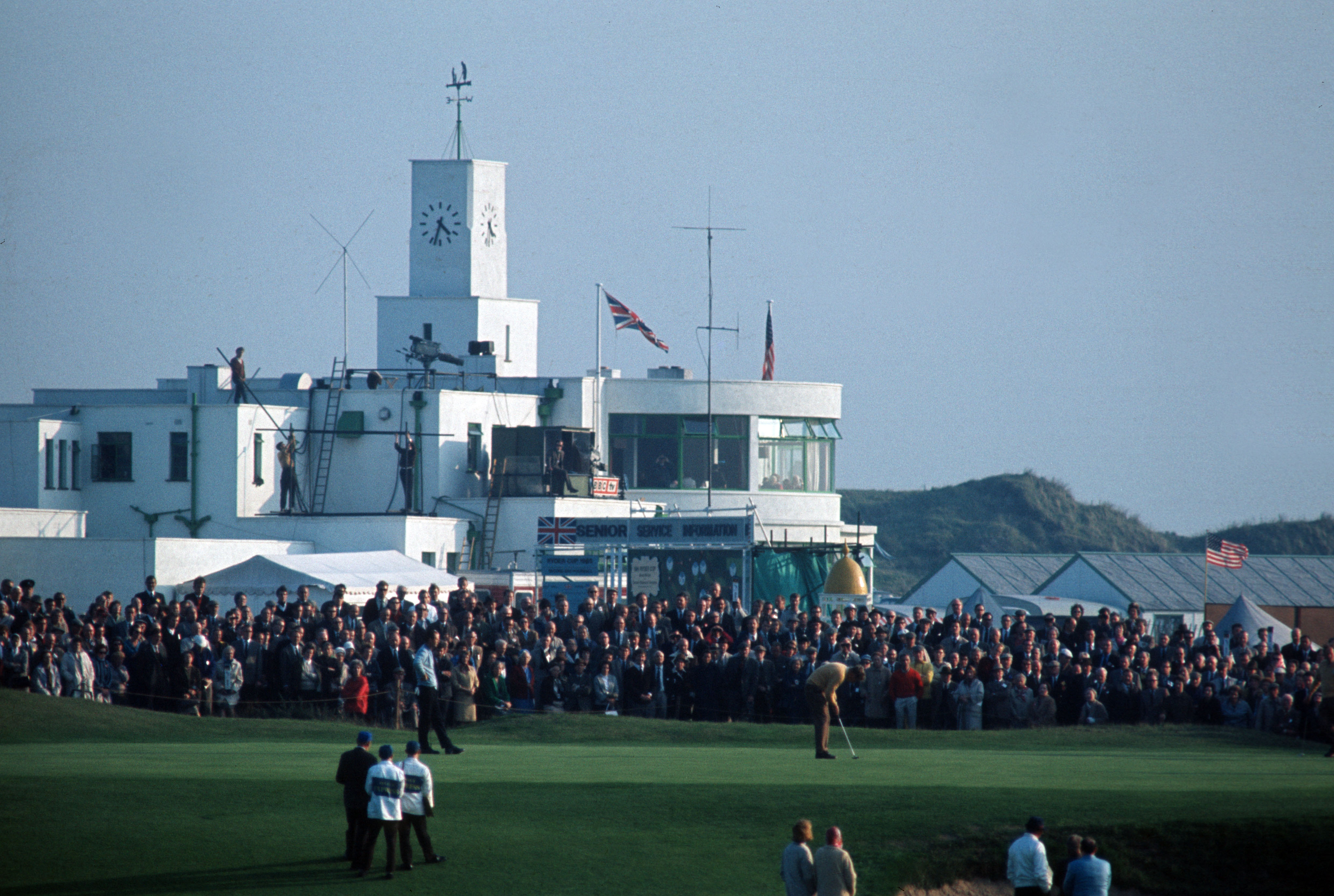 A golfer putts in front of a large crowd in front of the Royal Birkdale clubhouse at the 1965 Ryder Cup