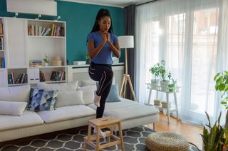 Woman using stool to perform step-up exercise at home