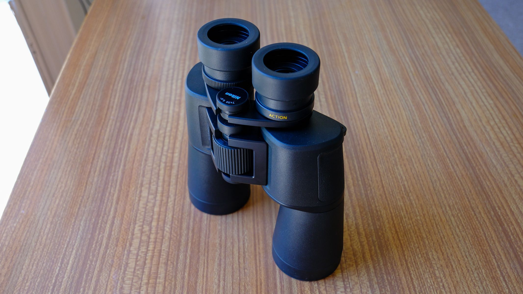 The Nikon Action 7x50 binoculars lens down stood up on a wooden table with eyecups fully extended.