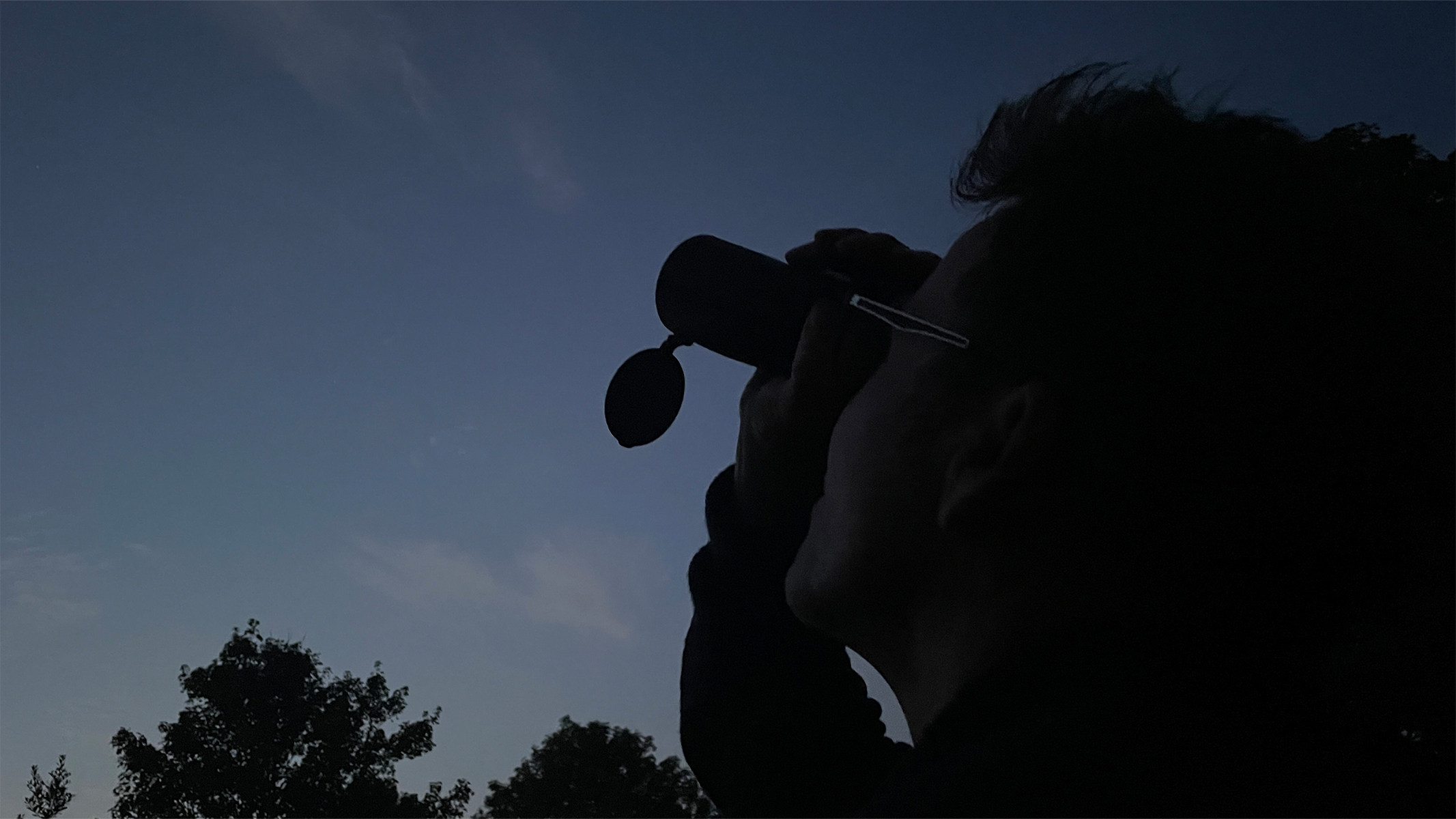 A man looking through a monocular at dusk.