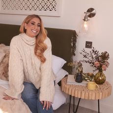 Stacey Solomon sad on bed next to wooden bedside table.