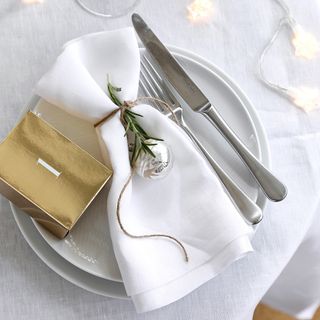 Christmas white folded napkin tied with twine and rosemary on white plates and cutlery with fairy lights